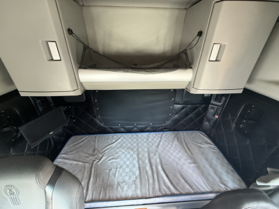 Kenworth W990 sleeper cab interior cargo area with quilted side panels, overhead storage cabinets, netted shelf, and a gray mat on the floor.
