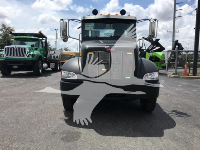 2022 Peterbilt 337 front view showing grille, headlights, and Peterbilt emblem with rollback truck dealership lot in background.