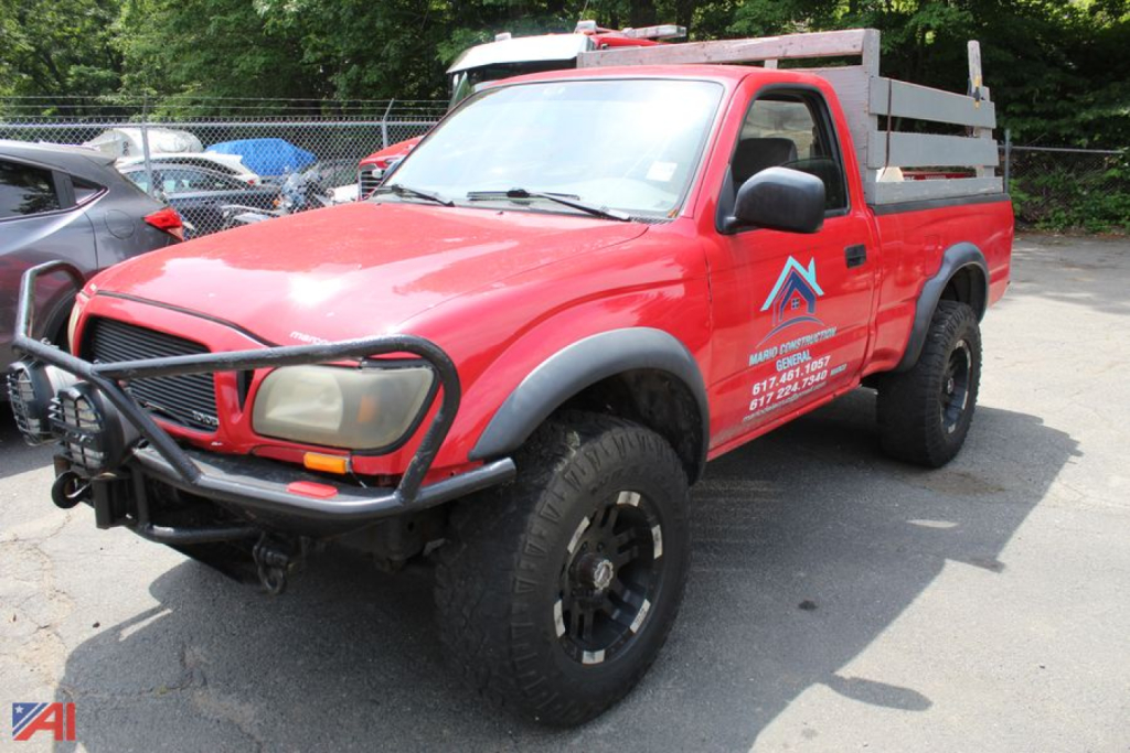 Red 2003 Toyota Tacoma pickup truck with utility bed and front grille guard, 4x4, side decals, and black off-road tires parked in lot.