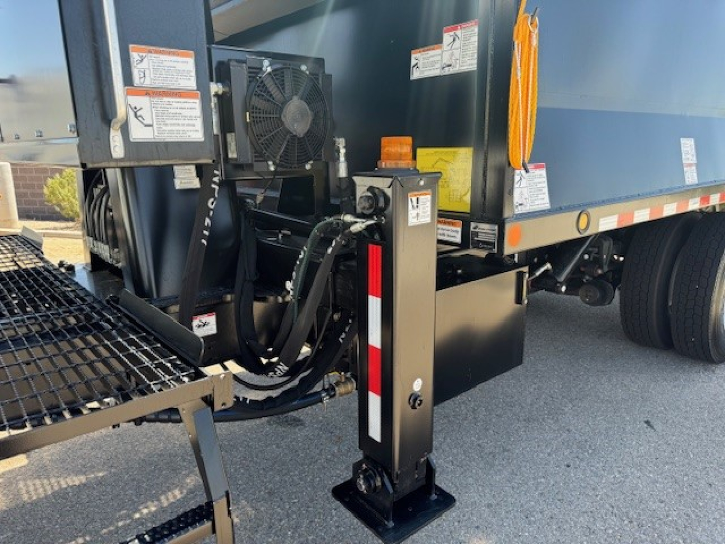 Front-right view of a 2024 Hino L7 grapple truck showing hydraulic outriggers, control panel, and side of the truck bed with label stickers.
