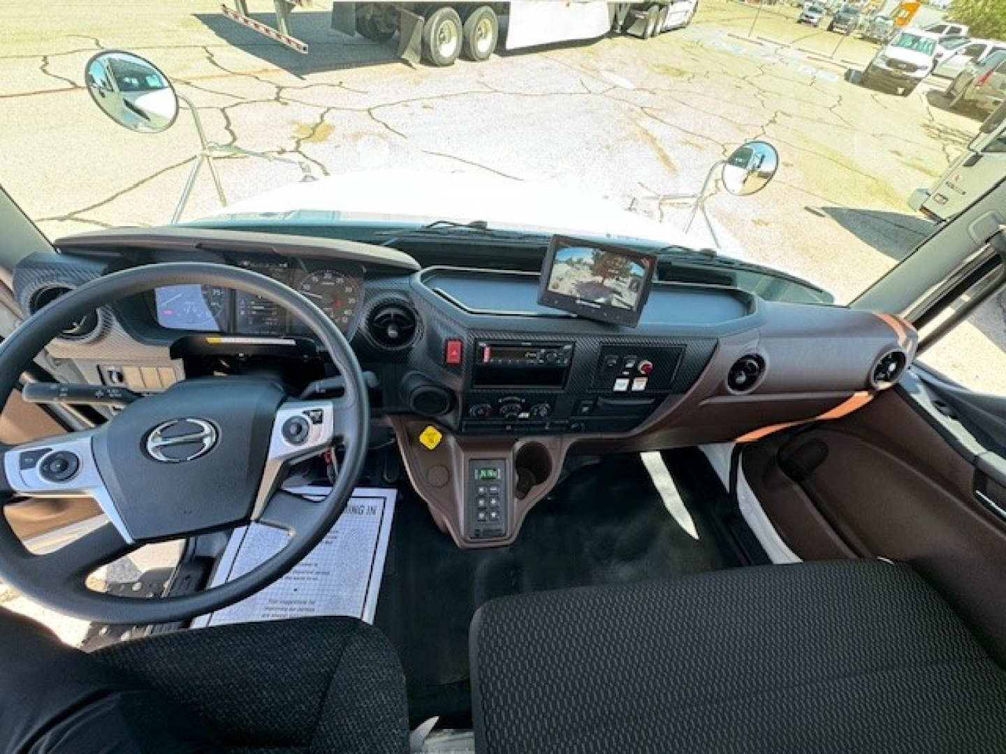Hino L7 cab interior showing steering wheel, dashboard, large center display, gear shifter, and control panels.