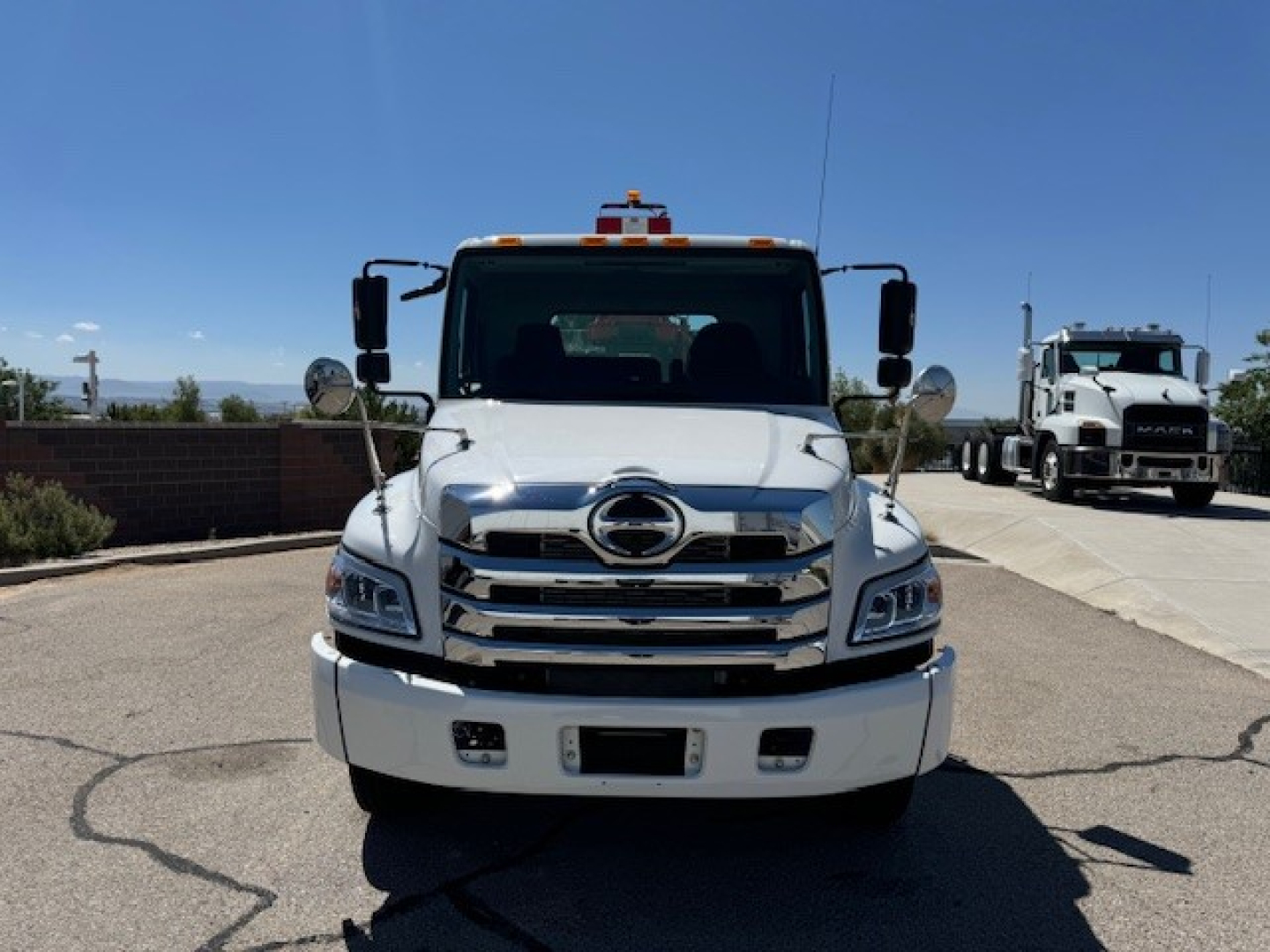 Front view of a white 2024 Hino L7 grapple truck showing chrome grille, Hino emblem, large bumper, dual headlights, side mirrors.
