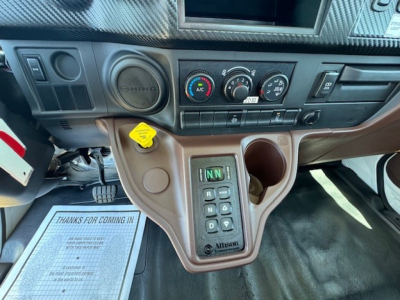 Control console and gear selector area of a 2024 Hino L7 grapple truck showing center stack with A/C controls, cup holder, and Allison transmission shifter.