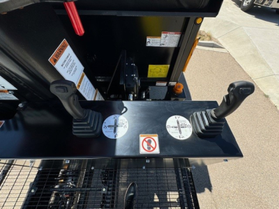 Operator controls area of a 2024 Hino L7 grapple truck showing two joysticks, control panel, warning decals, and hydraulic levers.