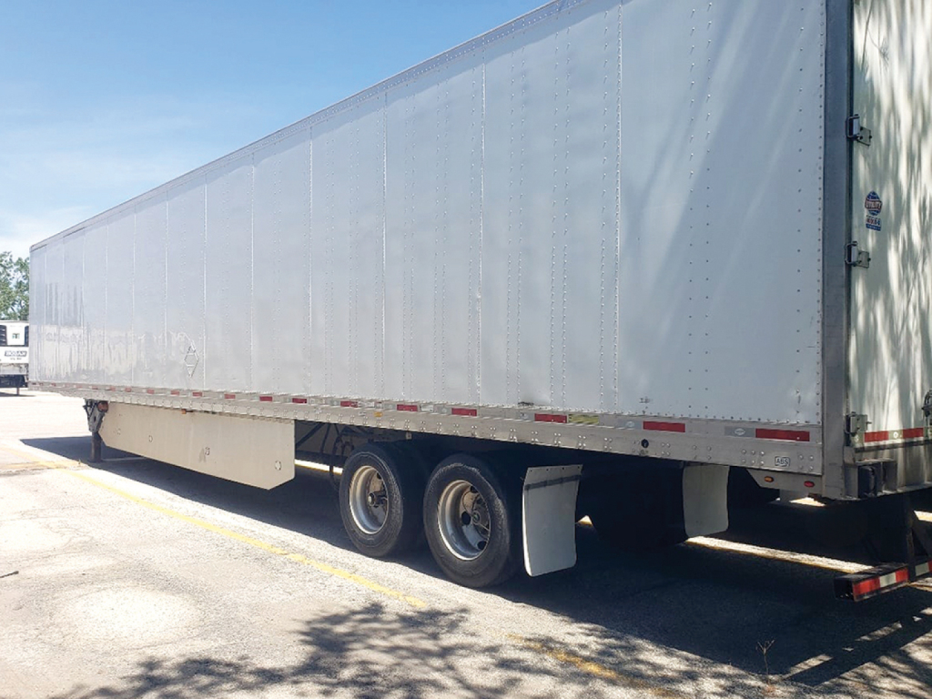 Trailer side view showing box trailer with dual rear axles and aluminum panels, undercarriage visible