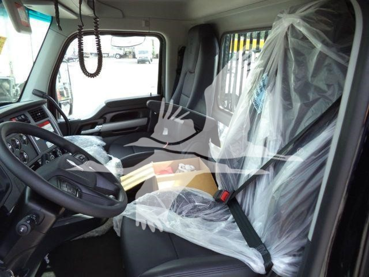 Kenworth T880 truck cab interior view with plastic seat covers and seat belts visible, steering wheel and dashboard in foreground.