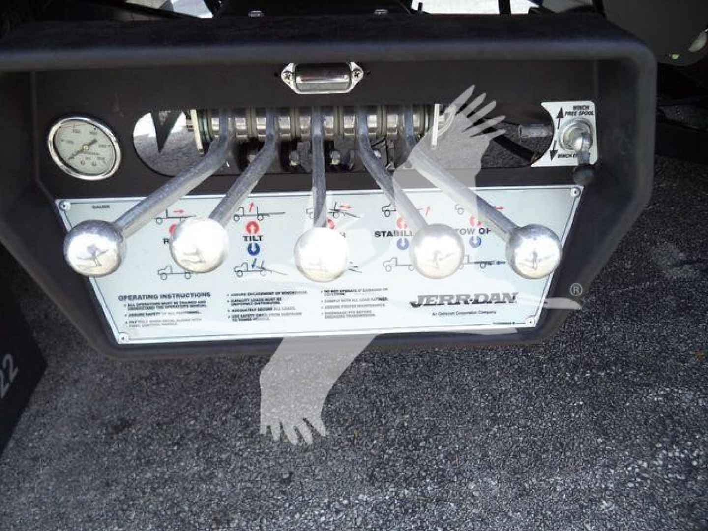 Kenworth T880 rollback control panel with multiple levers and an analog gauge, operating instructions plate labeled 'JER-...,' and a round dial on left.