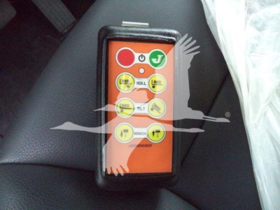 Remote control labeled with buttons: LIFT, ROLL, TILT, WINCH, PULL, plus symbols and icons; orange face with black border. Compact handheld control device.