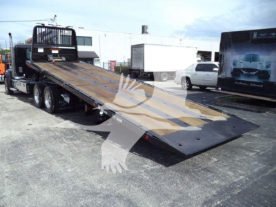 Kenworth T880 rollback truck with extended flatbed lowered to ground, text on side panels not legible.