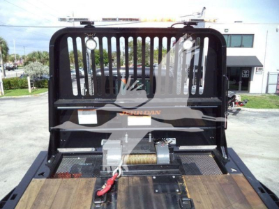 Kenworth T880 rollback truck bed with wood floor and hydraulic winch showing prominent grille and cage barrier