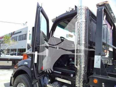 Kenworth T880 rollback truck cockpit with open door showing interior, metallic chrome exhaust stack, and crane/rack equipment in background.