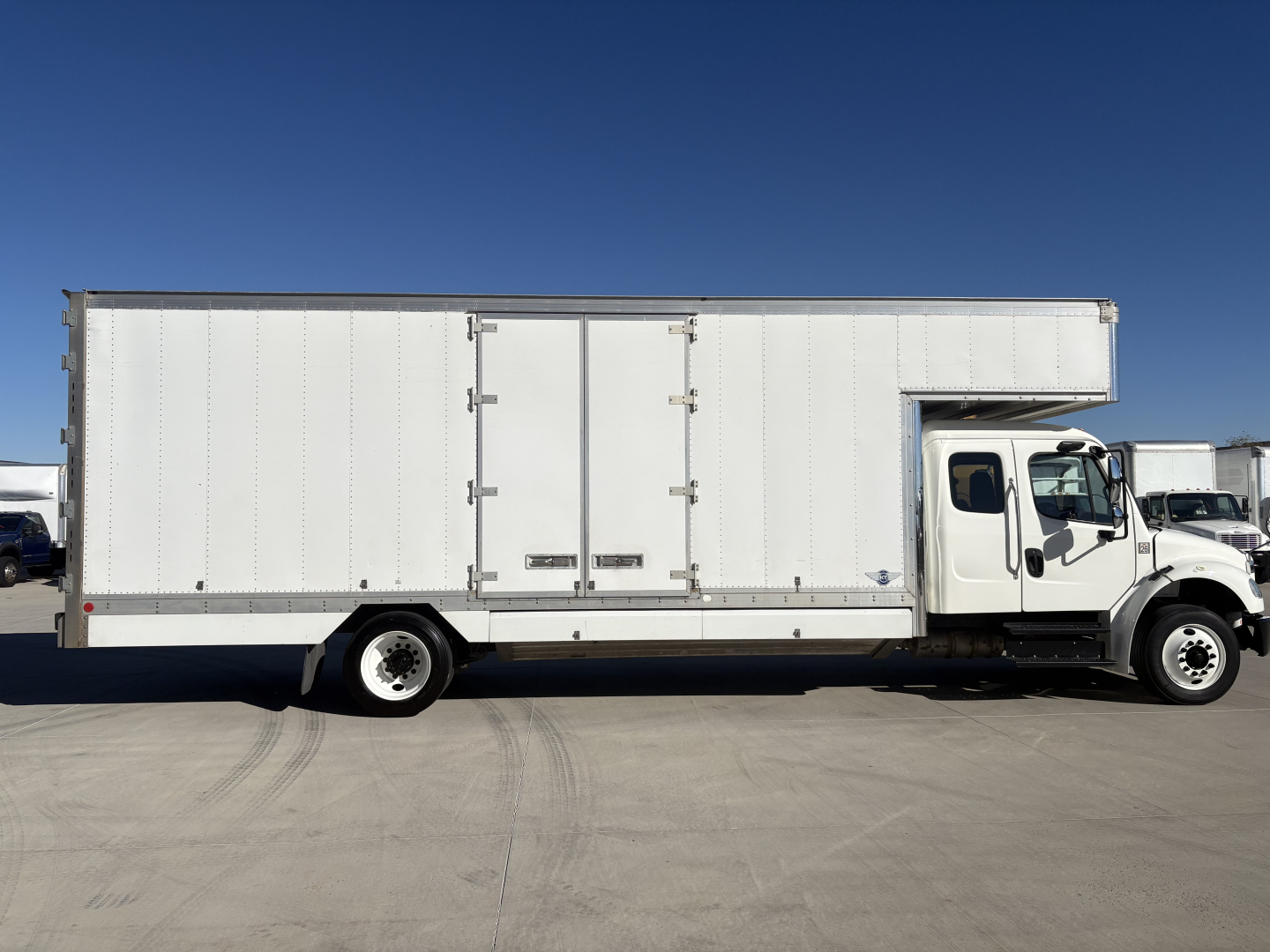 2019 Freightliner M2-106 box truck with a white cab and large box cargo area. Side view shows doors in the box and a single rear axle. No visible branding text readable on the truck body.