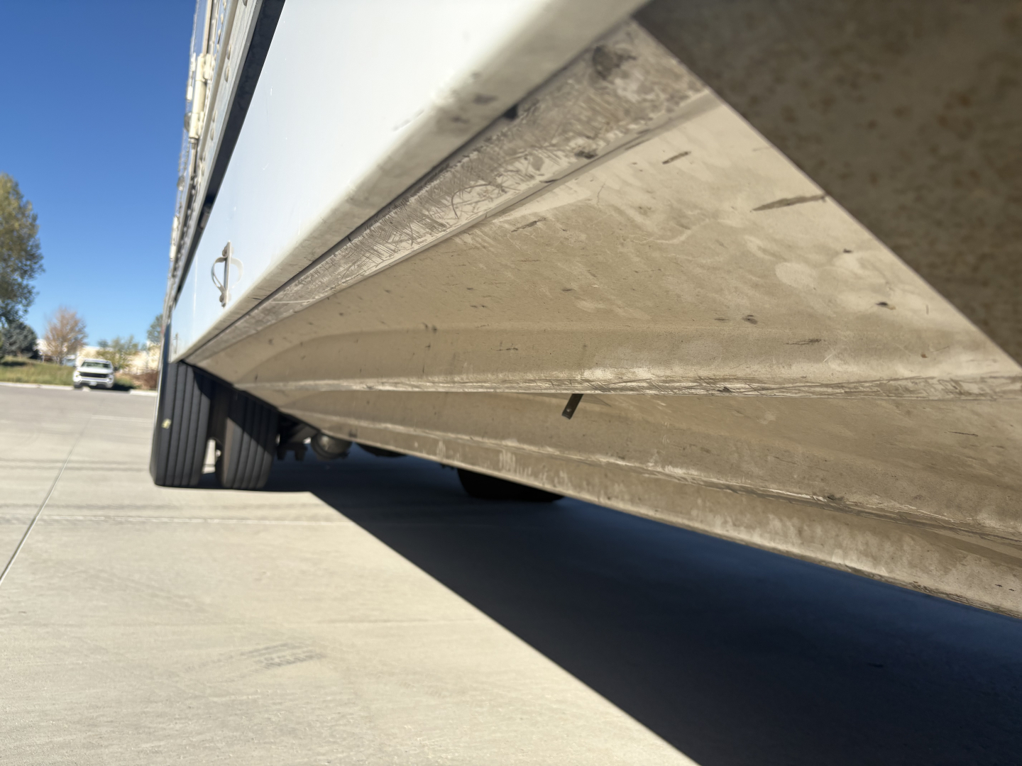 Low-angle side view of a Freightliner M2-106 box truck showing the undercarriage and wheel area with dirt on the lower side panel.