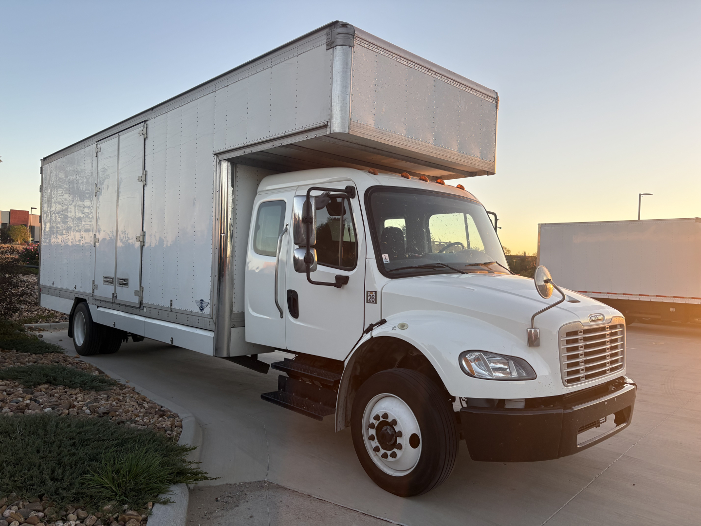 Box truck with raised box on Freightliner M2-106 cab; front grille, headlights, and side mirrors visible.
