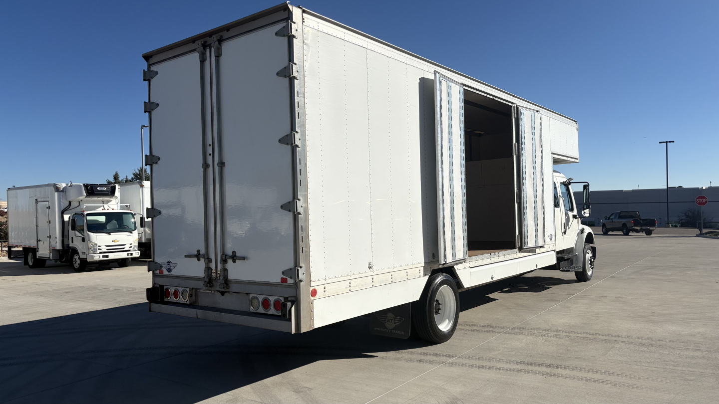 Box truck (2019 Freightliner M2-106) side and rear view showing large rear cargo doors open, white exterior, tandem rear wheels, cargo box, VIN 3ALACWFC9KDKX2173 not visible in image