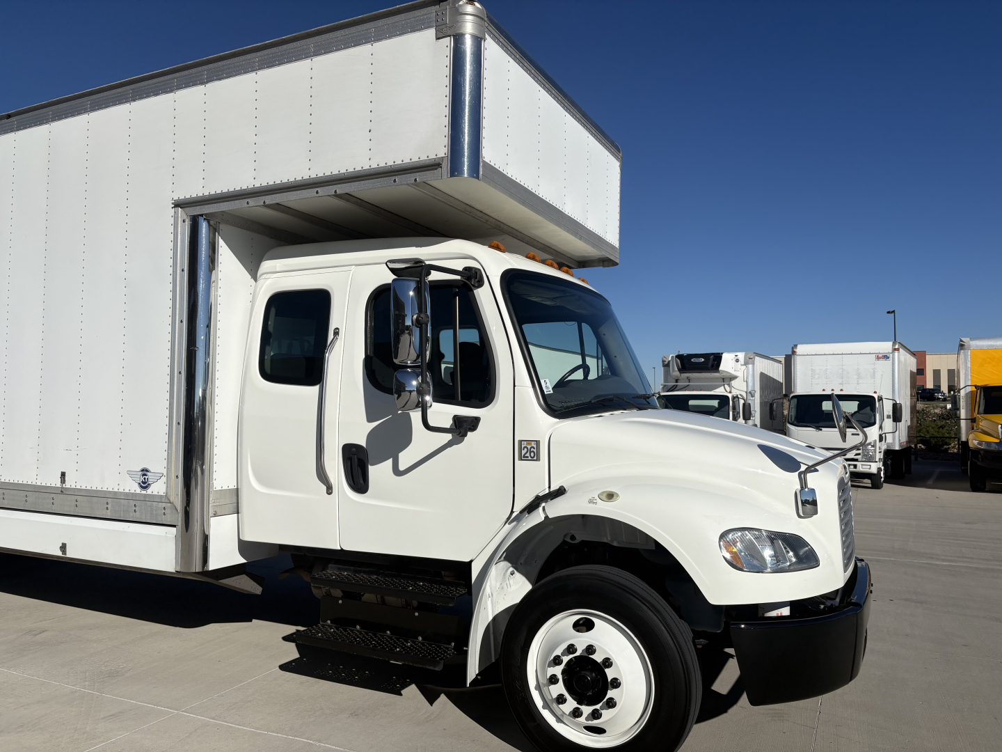 Vehicle side view of a 2019 Freightliner M2-106 box truck with inset cab doors and cargo box, showing front wheel and steps.