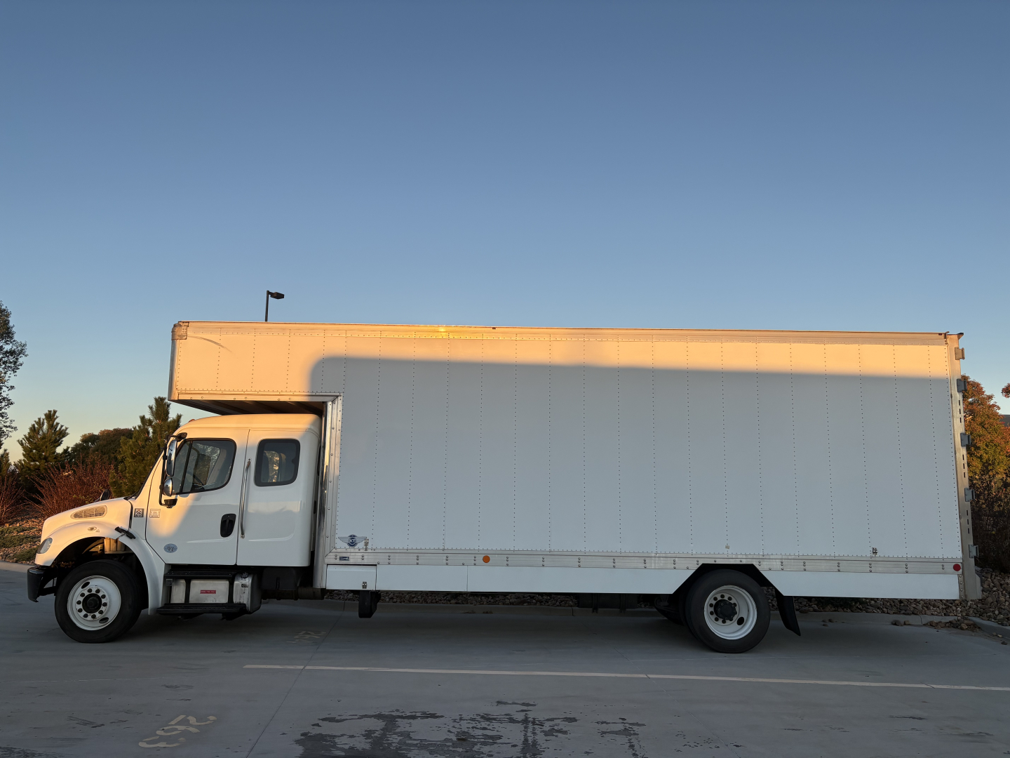 Freightliner M2-106 box truck side view showing long cargo box and cab, white exterior, on lot.