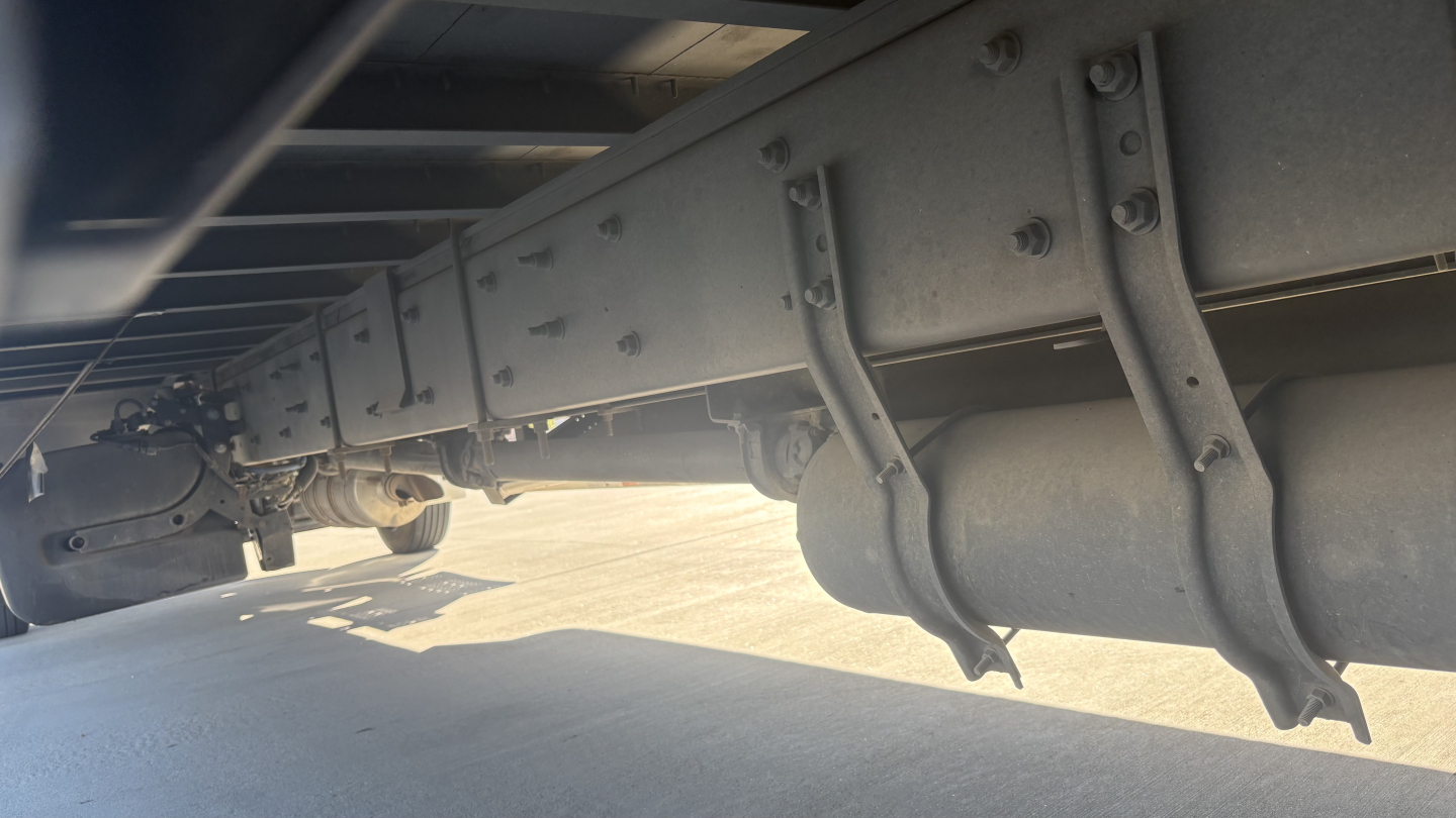 Underbody view of a Freightliner M2-106 truck showing chassis framing, suspension hangers, and undercarriage components.