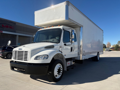 Box truck side view showing a white Freightliner M2-106 with a raised box on a daylight lot.