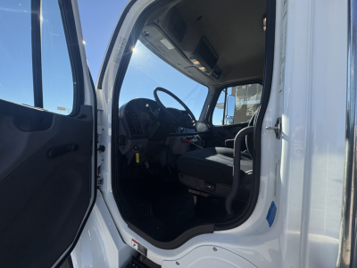 Freightliner M2-106 truck cab interior viewed from open door showing steering wheel, driver seat, pedals, and dashboard.
