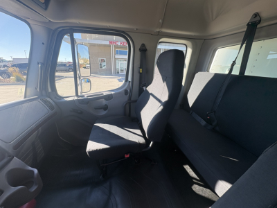 Freightliner M2-106 cab interior showing seating area and side window. Visible are driver seat, passenger bench, seat belts, and interior trim.