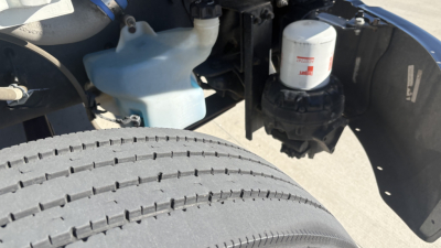 Freightliner M2-106 engine bay showing coolant reservoir, windshield washer bottle, and filter canister adjacent to a large front tire.
