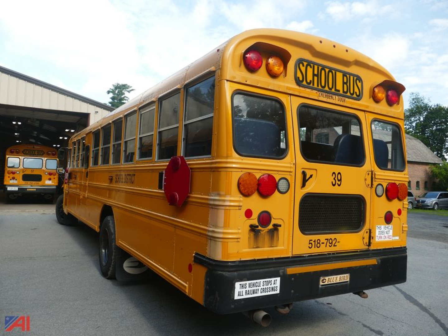 School bus rear view showing yellow body, red taillights, 'SCHOOL BUS' sign on the rear window, and a secondary bus in the background.