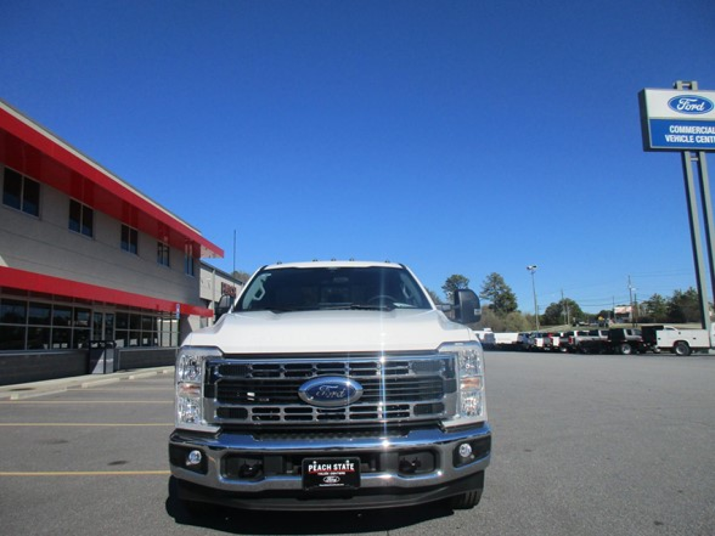 Front view of a white 2026 Ford F-350 Cab and Chassis truck in a dealership lot showing grille, Ford emblem, headlights, and bumper.