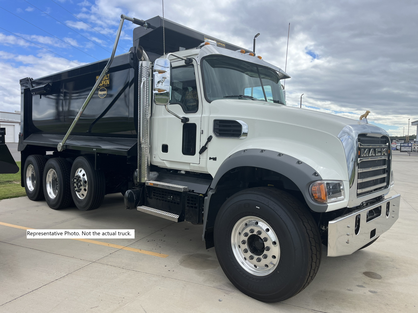 Dump truck front-right side view showing Mack GR84F dump truck with white cab and black dump bed, chrome bumper, large grille, dual rear wheels, and side steps.