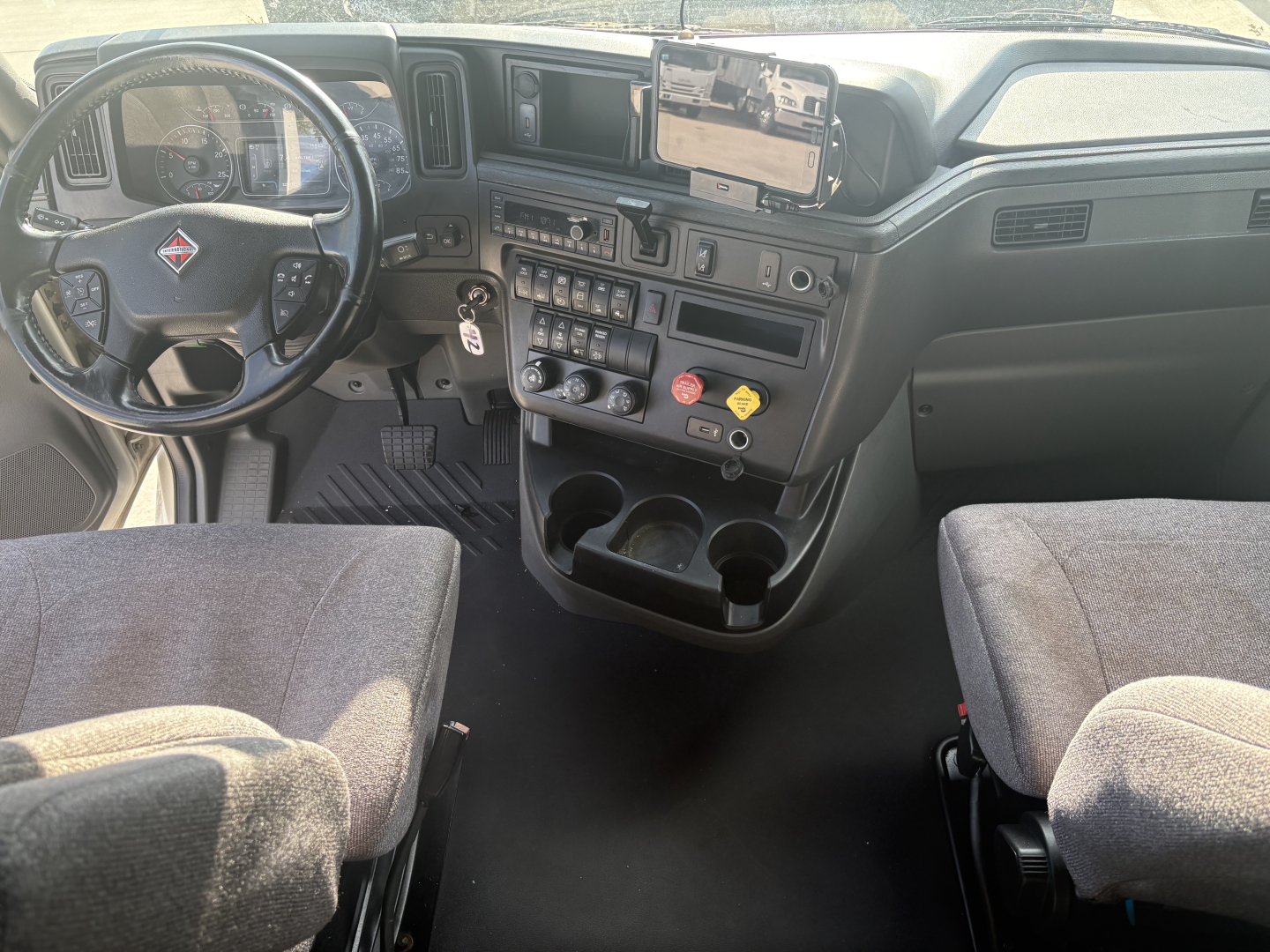 Interior of 2023 International LT625 truck cab showing steering wheel, dashboard with gauge cluster, center console with controls, cup holders, and driver/passenger seats.