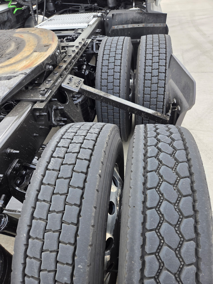 Truck rear dual axle configuration showing tires and suspension components under the cab, with drive shafts and frame visible.