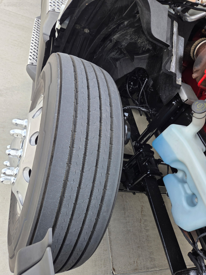 Wheel and front suspension of a 2023 International LT625 truck showing front dual wheels, tire tread, and blue coolant reservoir with surrounding engine bay components.