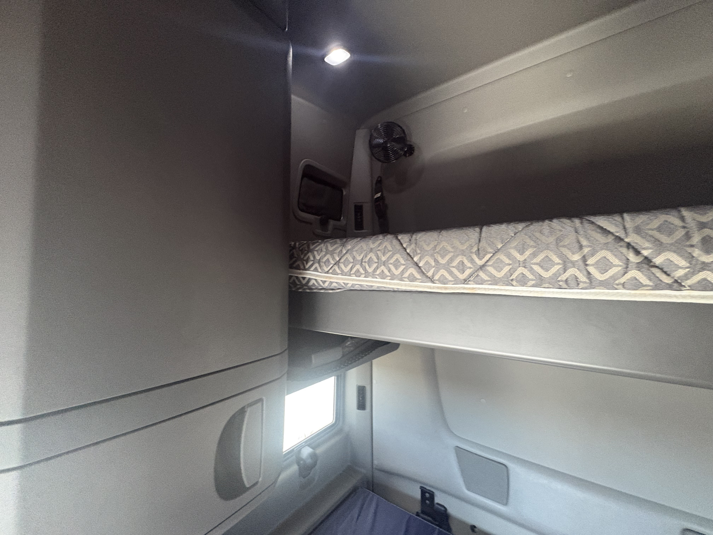 Interior sleeper cab bunk area of a used 2023 International LT625 showing upper bunk with patterned mattress, side paneling, and small window