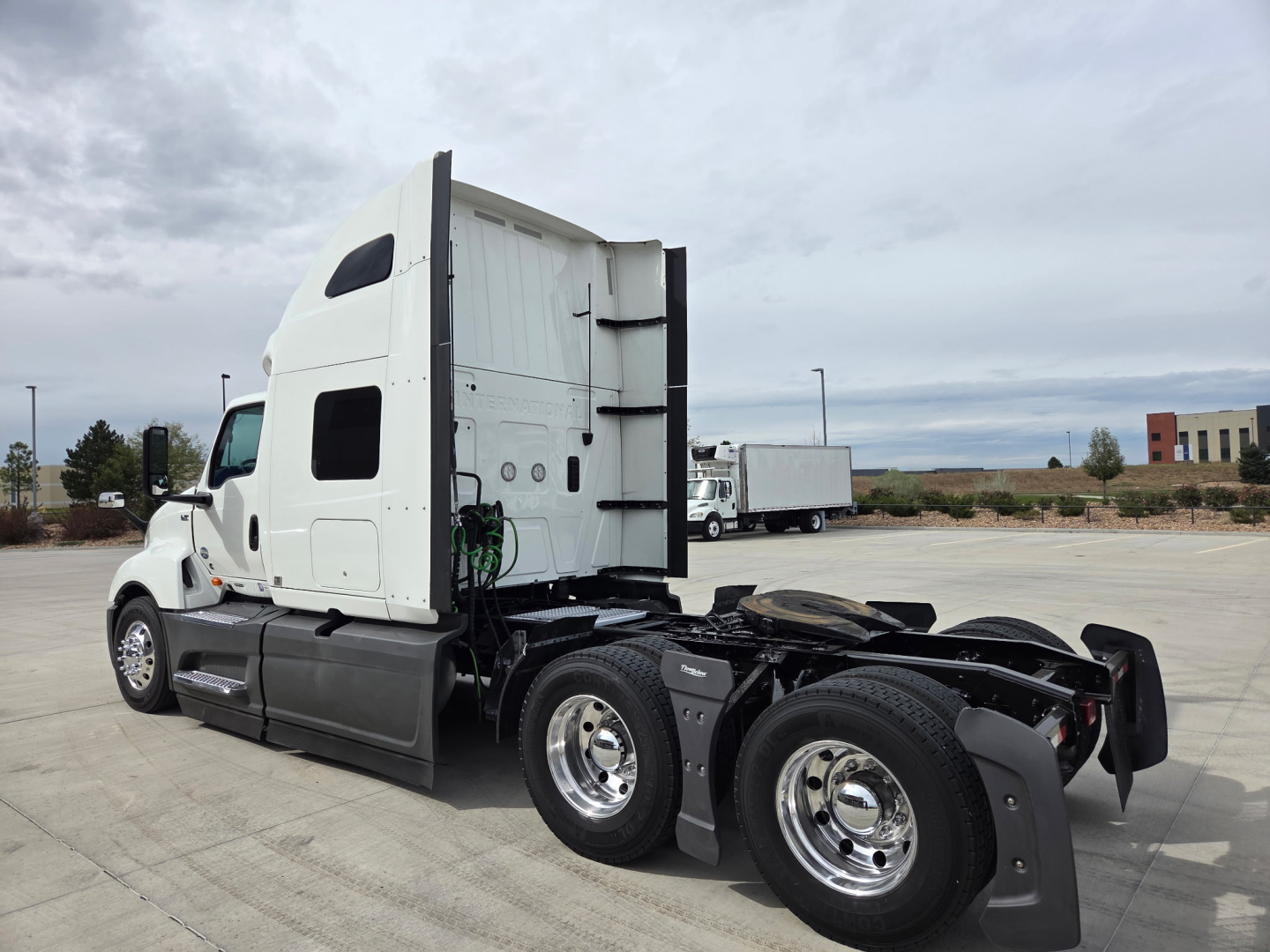 Truck rear shows fifth wheel and dual rear axles with white sleeper cab and chrome wheels.