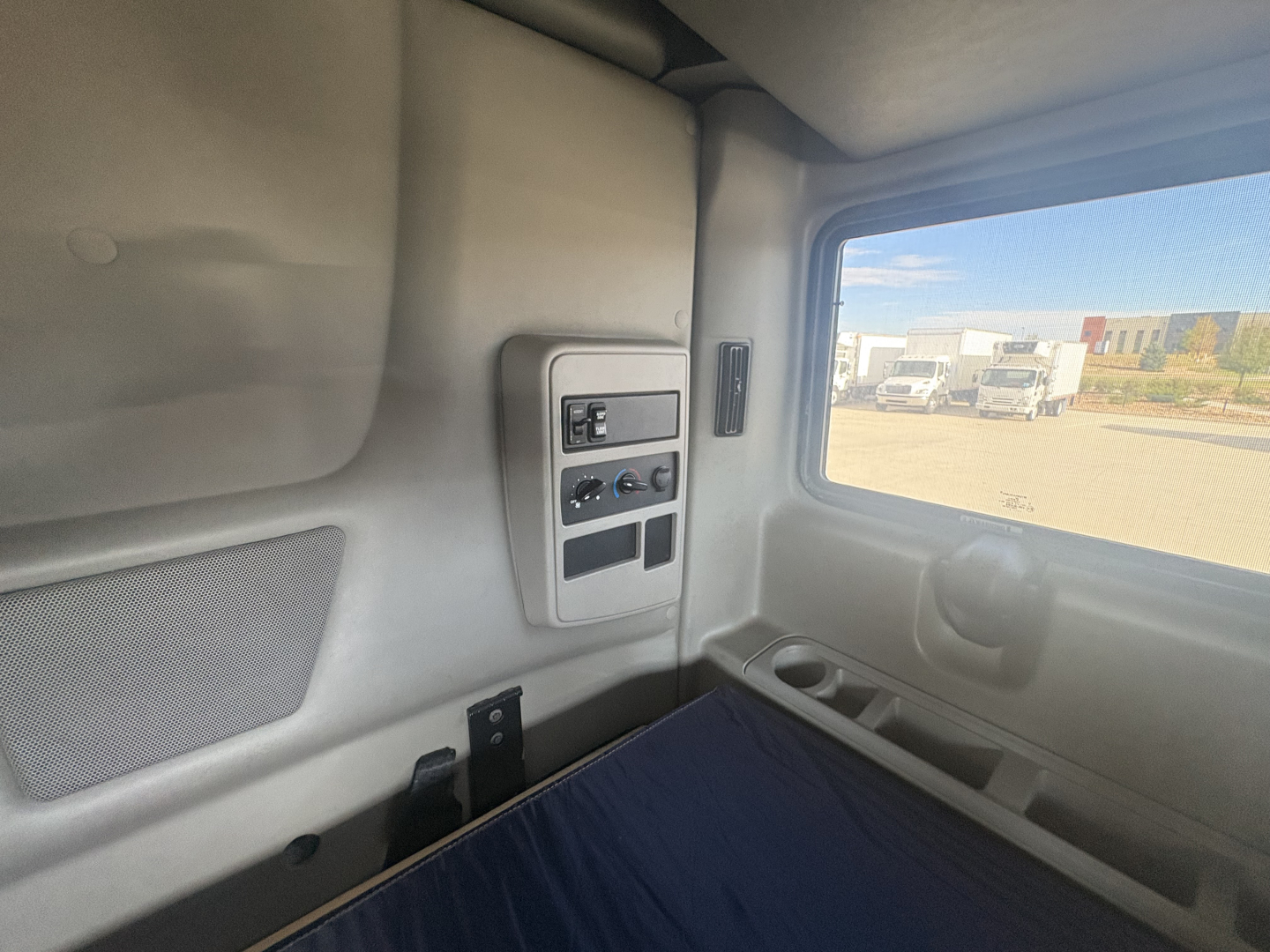 Cab interior of a 2023 International LT625 sleeper truck showing window, side panel with controls, storage pocket, and cup holder.