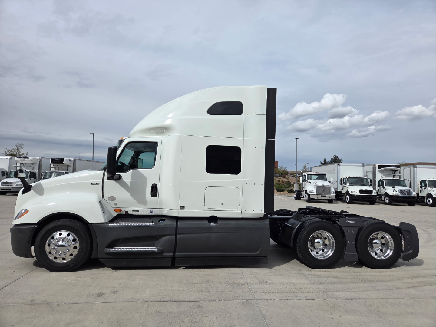 Truck side profile showing a white 2023 International LT625 tractor with sleeper, chrome wheels, and fuel tanks visible.
