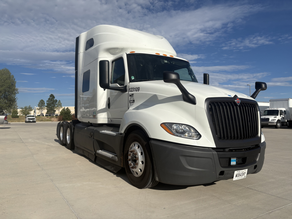 Truck cab with white International LT625 sleeper tractor, front grille and headlights, side mirrors, and dual rear axles visible.