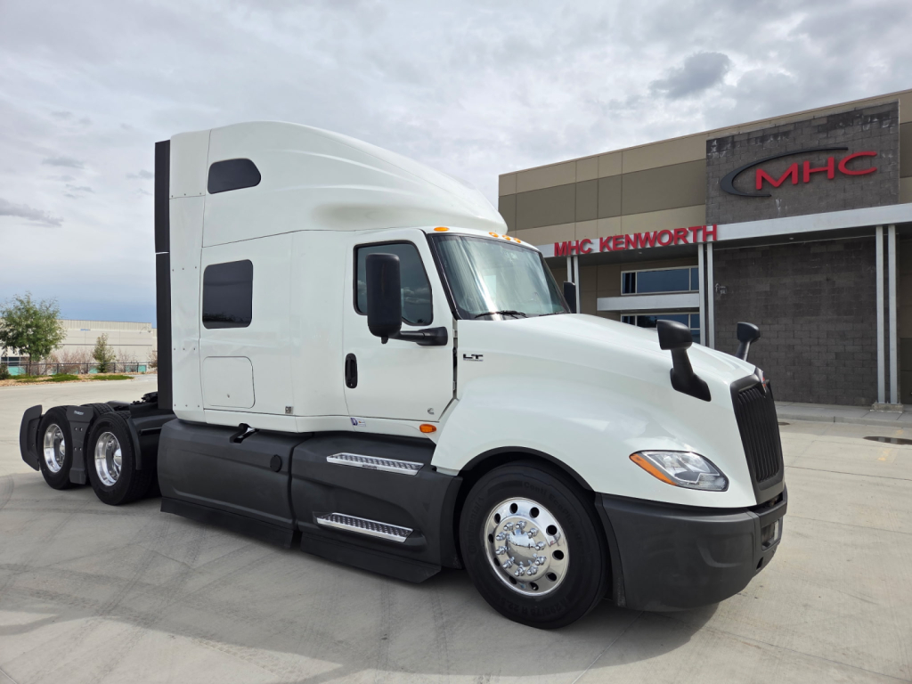 Semi truck tractor in a dealership lot showing International LT625 cab and sleeper with chrome wheels. Visible text includes MHC Kenworth building in background, no explicit model badges readable on truck side.