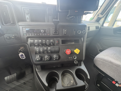 Cab interior of a truck showing dashboard controls, radio, multiple switches, climate controls, cup holders, and a passenger seat.