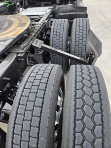 Truck rear dual axle configuration showing tires and suspension components under the cab, with drive shafts and frame visible.