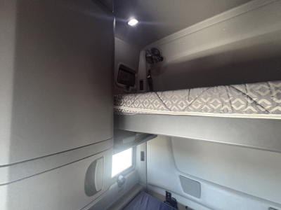 Interior sleeper cab bunk area of a used 2023 International LT625 showing upper bunk with patterned mattress, side paneling, and small window