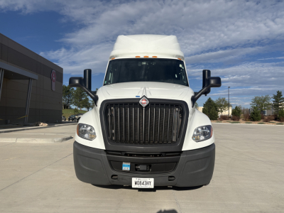 Front view of a white 2023 International LT625 conventional sleeper truck showing large black grille, bumper, headlights, side mirrors, and a license plate.