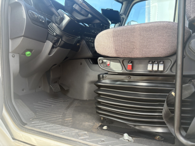 Interior view of a truck cab showing driver seat, dashboard controls, and a ribbed pedestal with a red switch panel.
