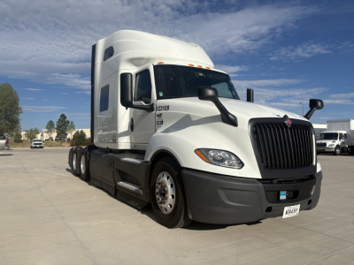Truck cab with white International LT625 sleeper tractor, front grille and headlights, side mirrors, and dual rear axles visible.