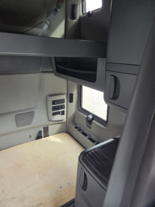 Interior of a truck sleeper cab with a small desk shelf, window, and controls; no visible text in the photo.