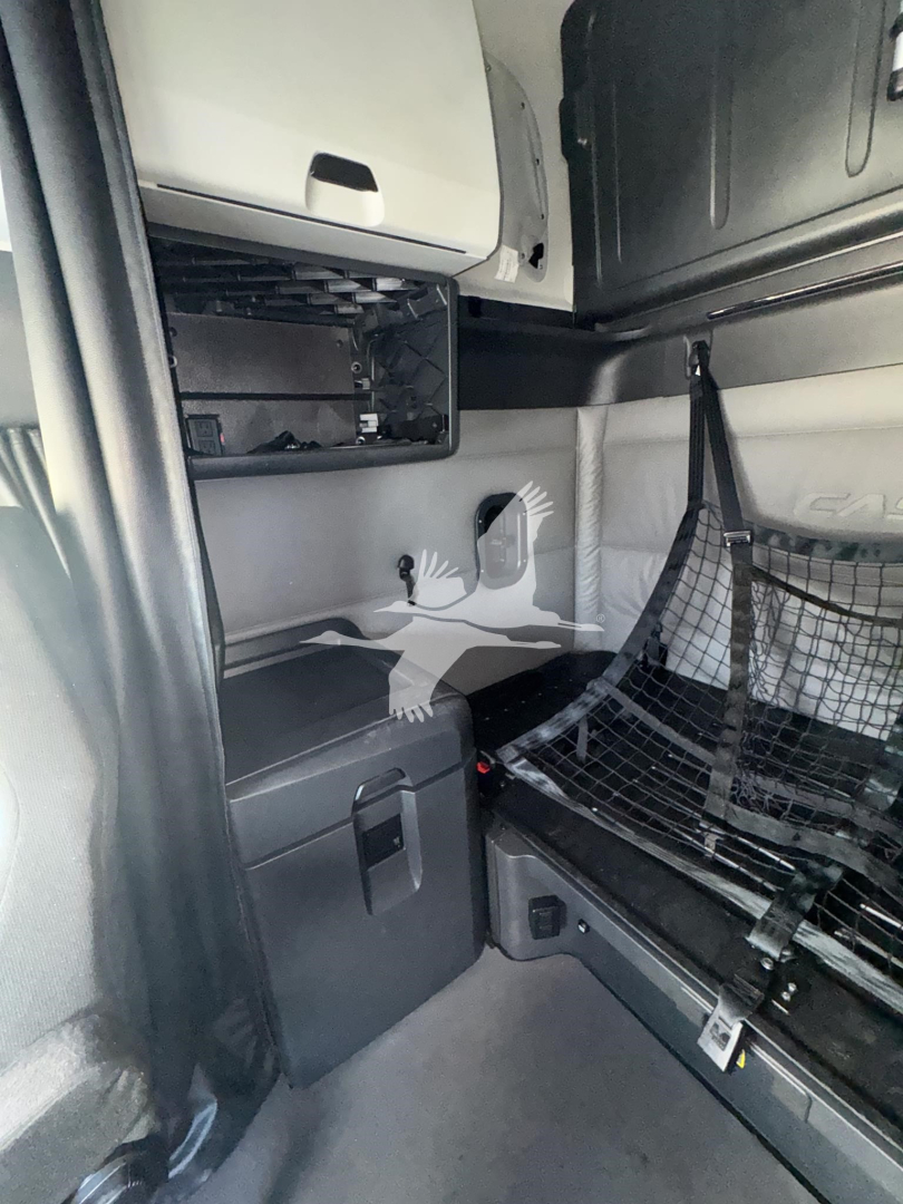 Interior cab of a used 2023 Freightliner Cascadia 126 showing sleeper area with storage shelves, a net cargo barrier, and a small cabinet.
