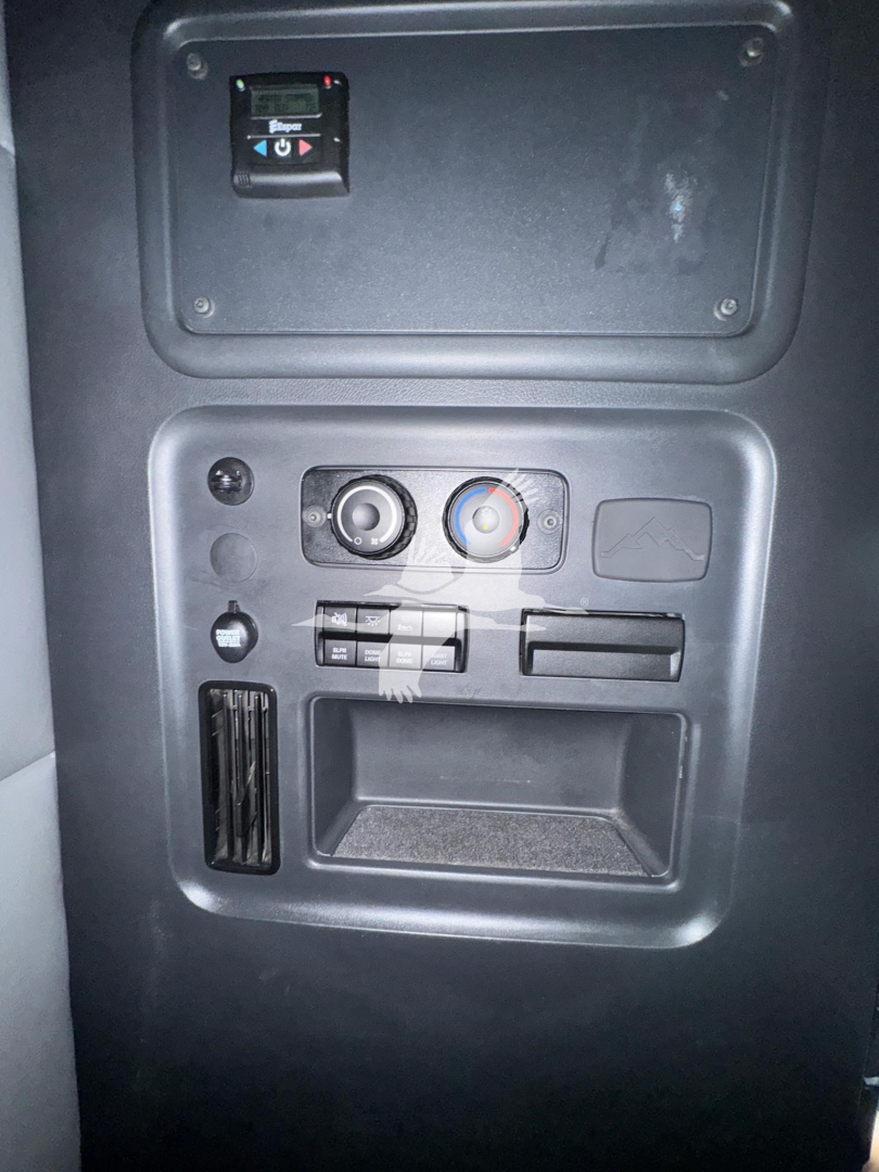 Dashboard panel with switches and circular dials and a small storage pocket in a Freightliner Cascadia cab interior. Visible are two round knobs, a red/blue climate control ring, a few toggle switches, and a small empty tray.