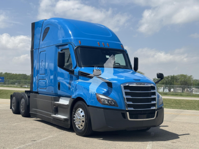 Truck cab of a blue 2023 Freightliner Cascadia 126, three-axle tractor, side view with chrome grille and aerodynamic body kit.