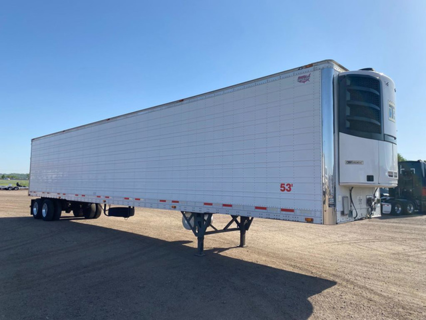 Trailer in-side view showing a 53' reefer with its refrigeration unit at the front, white insulated walls, tri-axle configuration, and landing gear extended.
