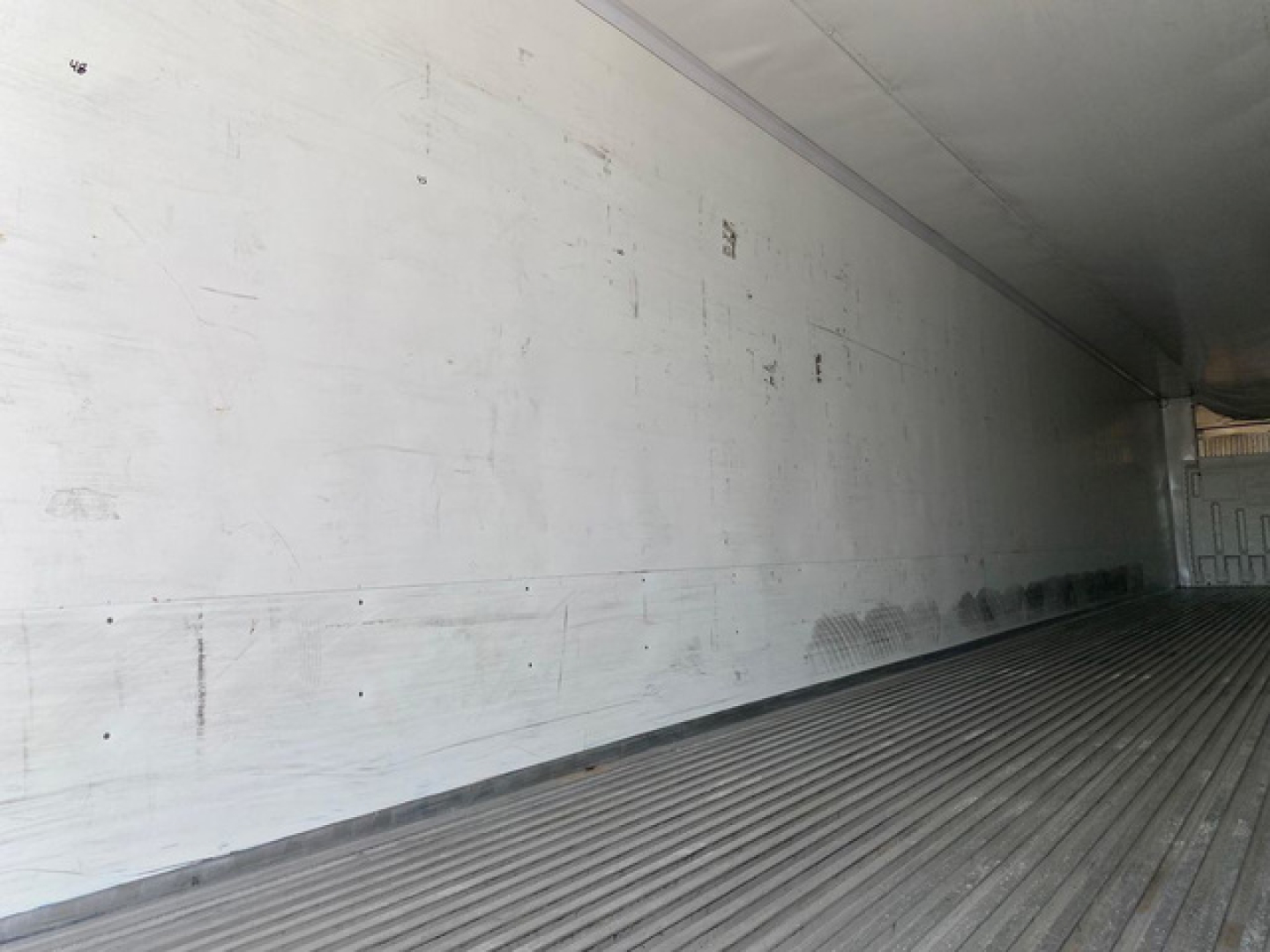 Trailer interior showing ribbed metal floor and white sidewalls with scuffs; empty refrigerated trailer cargo area interior.